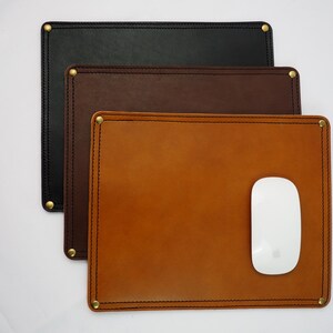 May include: Three leather mouse pads in different colors: black, brown, and tan. The tan mouse pad has a white computer mouse on top of it.