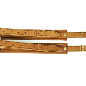 May include: Two brown leather straps with brass buckles and clasps. The straps are stitched together and have a decorative pattern.