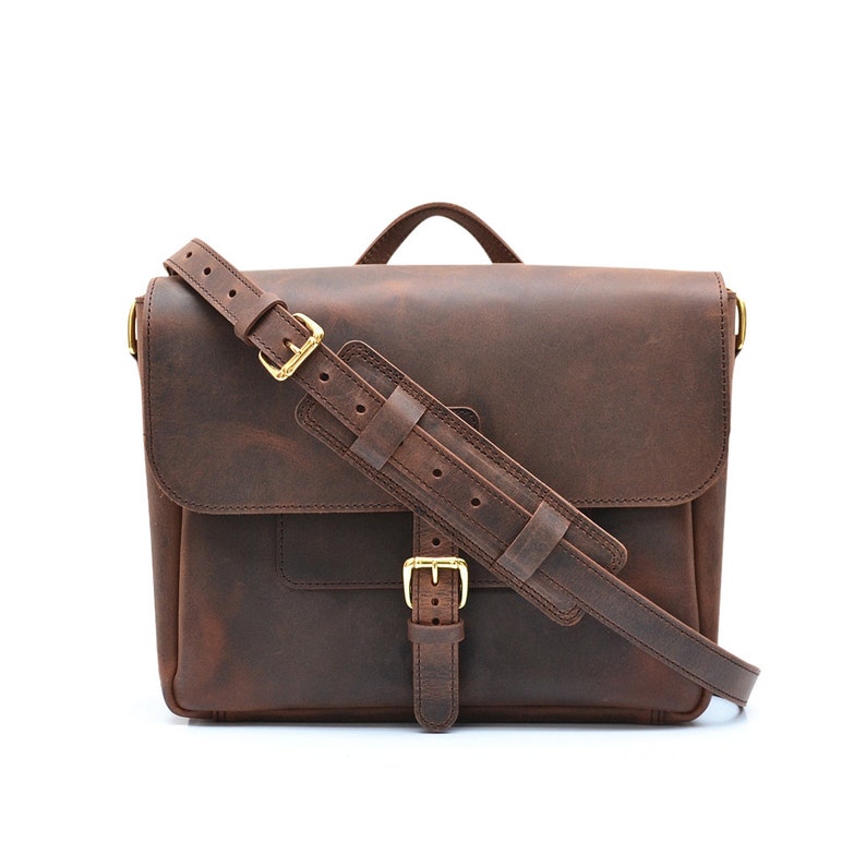 May include: A brown leather messenger bag with a flap closure, adjustable shoulder strap, and a top handle. The bag features gold-coloured buckles and hardware. The leather has a distressed appearance.