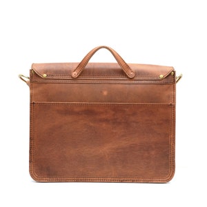 May include: A brown leather briefcase with a top handle and a front pocket. The bag features brass-coloured hardware and a flap closure. The leather has a distressed appearance.
