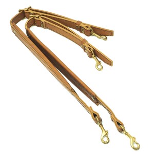 May include: Three brown leather straps with gold metal clasps and hooks. The straps are connected together and are ready to be attached to a bag or other item.