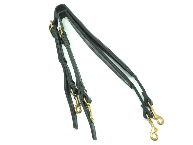May include: A pair of black leather shoulder straps with gold metal clasps and hooks.