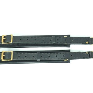 May include: Two black leather straps with gold metal buckles and clasps. The straps have a series of small holes along their length.