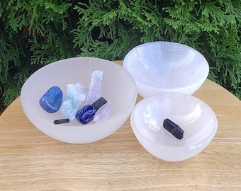 May include: Three selenite bowls, one larger than the other two, with a variety of crystals and stones inside. The bowls are white and have a frosted finish. The crystals are blue, pink, and black.