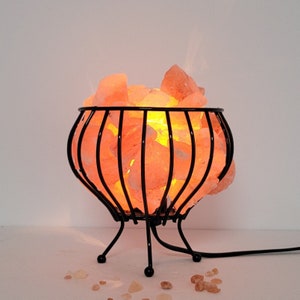 May include: A Himalayan salt lamp in a black metal cage with a round base and three legs. The salt crystals are glowing orange.