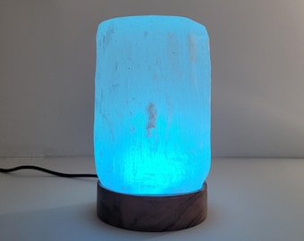 May include: A blue Himalayan salt lamp with a wooden base. The lamp is lit and emitting a soft blue glow.