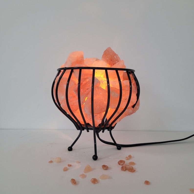 May include: A Himalayan salt lamp with a black metal cage base. The salt crystals are glowing orange and the lamp is plugged in.