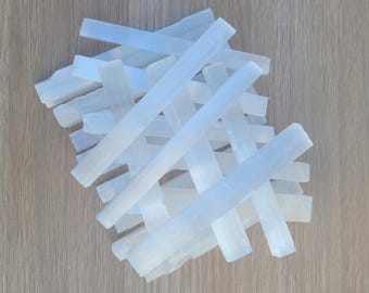 May include: A pile of white selenite wands, also known as selenite sticks, on a wooden surface. The wands are smooth and polished, with a translucent appearance.