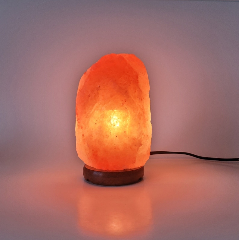 May include: A warm, orange-toned Himalayan salt lamp with a wooden base. The lamp is lit and glowing.