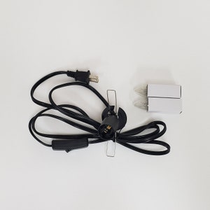 Pu&ograve; includere: Un cavo elettrico nero con una spina, un interruttore in linea e una presa per lampadina. Il cavo &egrave; avvolto e la presa &egrave; fissata a una base metallica. Sono incluse due lampadine di ricambio.