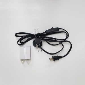 Pu&ograve; includere: Un cavo elettrico nero con una spina, un interruttore in linea e una presa per una lampadina. Due lampadine di ricambio sono incluse nell'immagine.