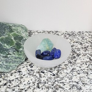 Pu&ograve; includere: Una ciotola bianca piena di cristalli blu e verdi. La ciotola &egrave; su una superficie macchiata di grigio e bianco.