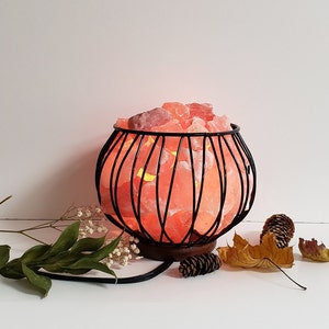 May include: A Himalayan salt lamp in a black metal cage. The salt crystals are glowing orange and the lamp is sitting on a wooden base.