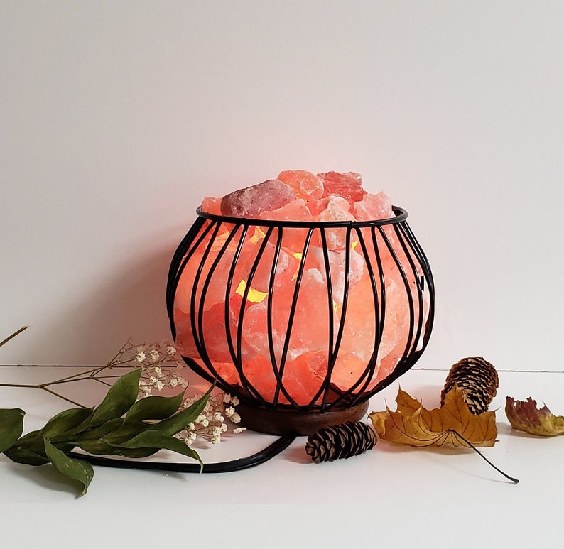 May include: A Himalayan salt lamp in a black metal cage. The salt crystals are glowing orange and the lamp is sitting on a wooden base.