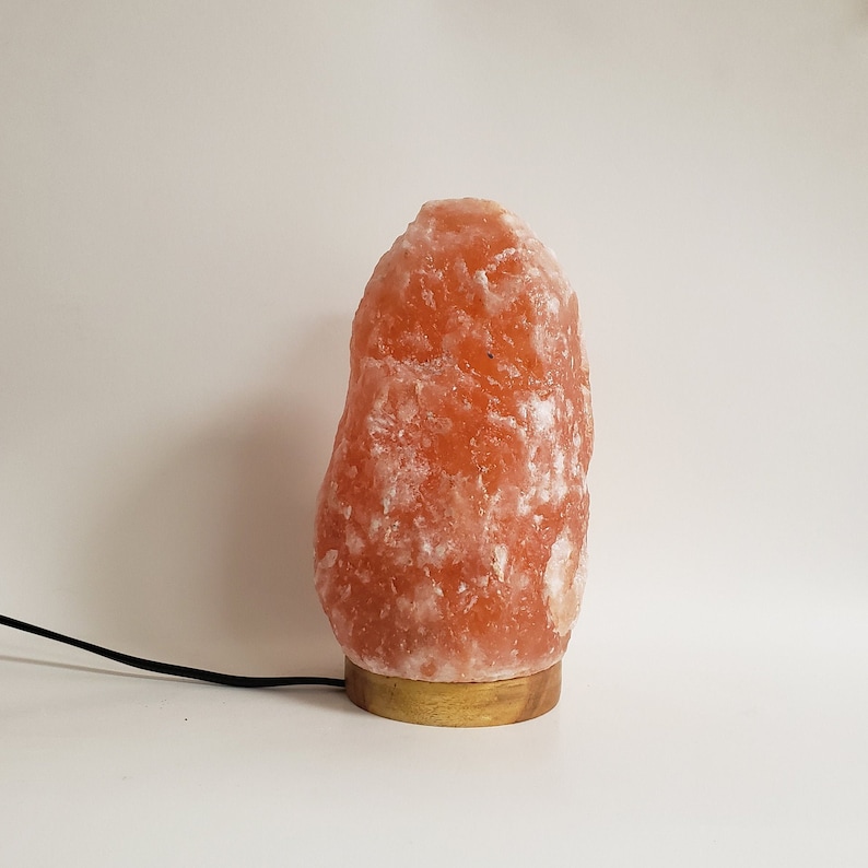 May include: A Himalayan salt lamp with a natural, orange-pink hue. The lamp is on a wooden base and has a cord.