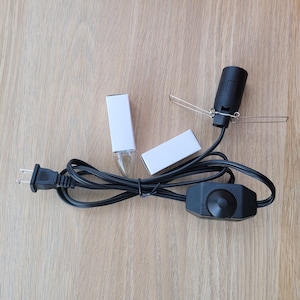 May include: A black electrical cord with a plug on one end and a light socket on the other. The cord has a black inline dimmer switch with a knob. Two white boxes are included.