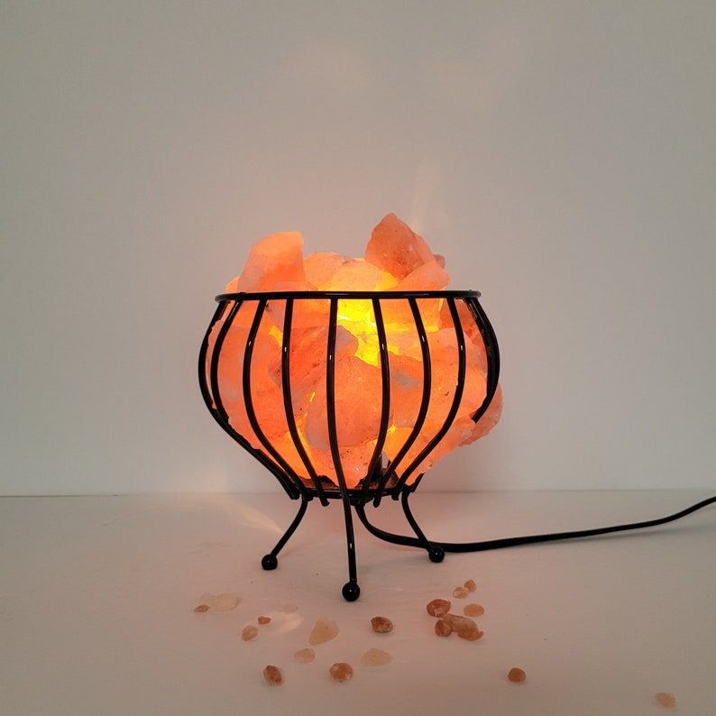 May include: A Himalayan salt lamp with a black metal cage base. The salt crystals are glowing orange from the light inside.