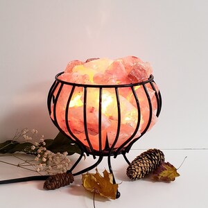 May include: A Himalayan salt lamp in a black metal cage with a round base. The salt crystals are illuminated from within, creating a warm glow.
