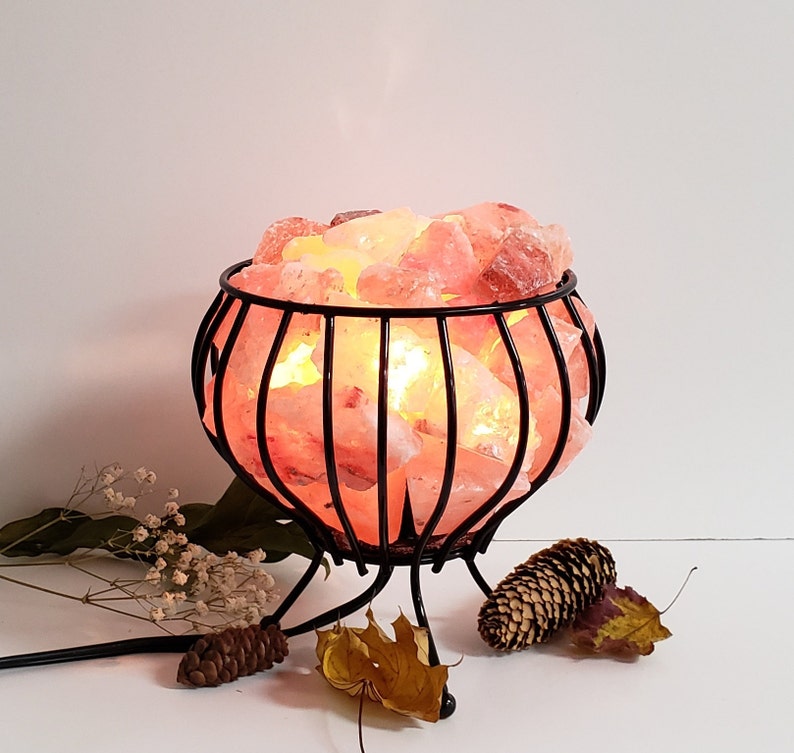 May include: A Himalayan salt lamp in a black metal cage with a round base. The salt crystals are illuminated from within, creating a warm glow.
