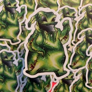 May include: A sticker depicting a green character with a stitched appearance and a wide grin. The character has a starry, galaxy-like pattern within its body. Similar stickers surround the main image. The design has a whimsical, cartoonish style.