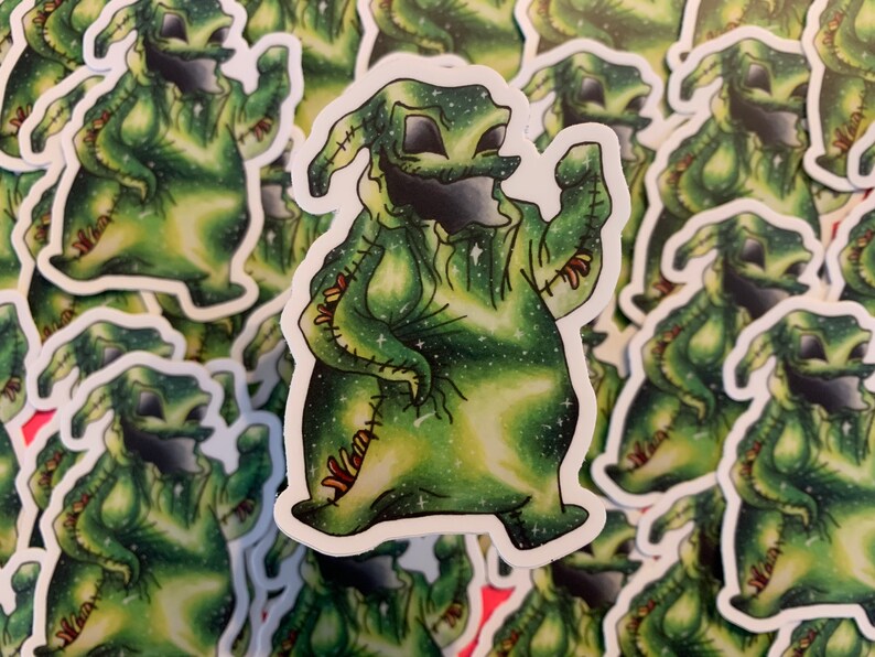 May include: A sticker depicting a green character with a stitched appearance and a wide grin. The character has a starry, galaxy-like pattern within its body. Similar stickers surround the main image. The design has a whimsical, cartoonish style.