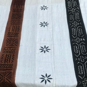 May include: White fabric with brown and black patterned borders. The fabric has a series of black star-shaped designs.
