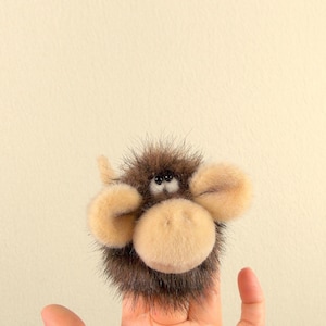 May include: A brown and tan furry finger puppet with black eyes and a large, round nose.