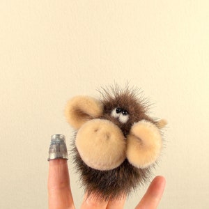 Puede incluir: Un t&iacute;tere de dedo peludo marr&oacute;n y beige con ojos negros. El t&iacute;tere est&aacute; en un dedo y parece un animal peque&ntilde;o.