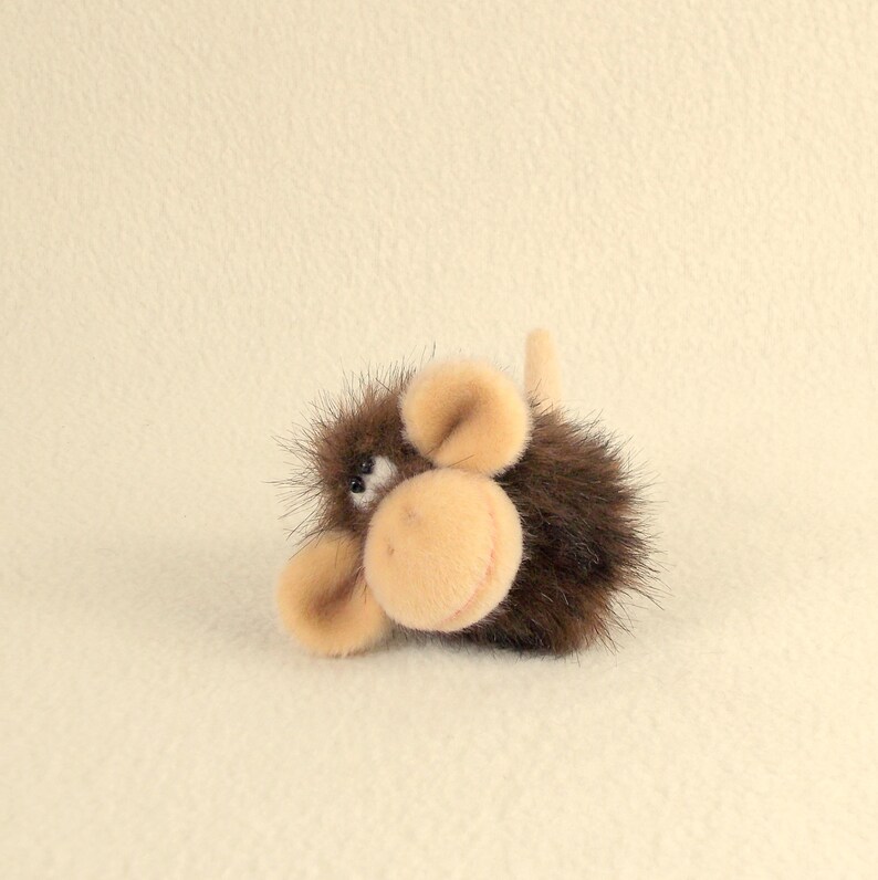 Puede incluir: Un juguete de peluche de mono marr&oacute;n y beige con textura peluda. El mono tiene una peque&ntilde;a nariz negra y ojos grandes y negros.