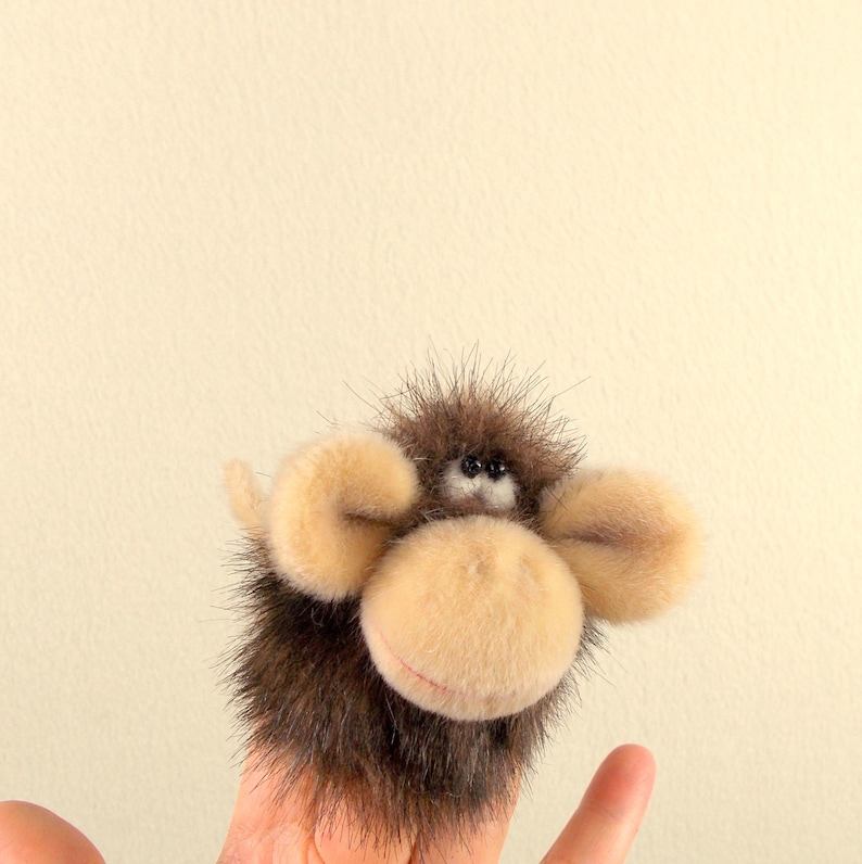 Puede incluir: Un t&iacute;tere de dedo de peluche marr&oacute;n y beige con orejas grandes y ojos negros. El t&iacute;tere est&aacute; hecho para parecer un mono.