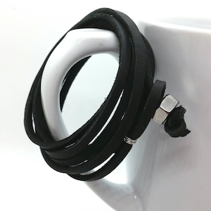 May include: Black leather wrap bracelet with a silver metal clasp. The bracelet is wrapped around a white mug.