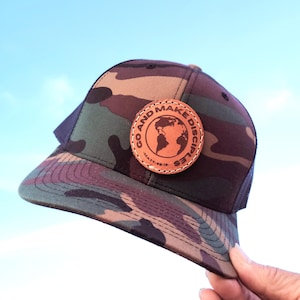 May include: A camouflage trucker hat with a brown leather patch that says "Go and Make Disciples" with a globe graphic and the scripture reference "Matt 28:19-20".