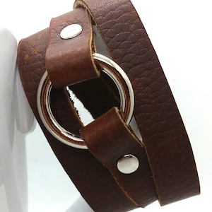May include: A brown leather wrap bracelet with a silver ring and two silver snaps.