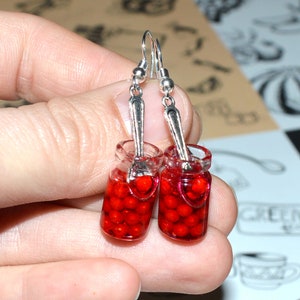 May include: A pair of silver dangle earrings featuring miniature glass jars filled with red cherries and a silver spoon charm.