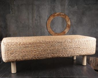 May include: A natural woven rectangular ottoman with a light brown color and four wooden legs.