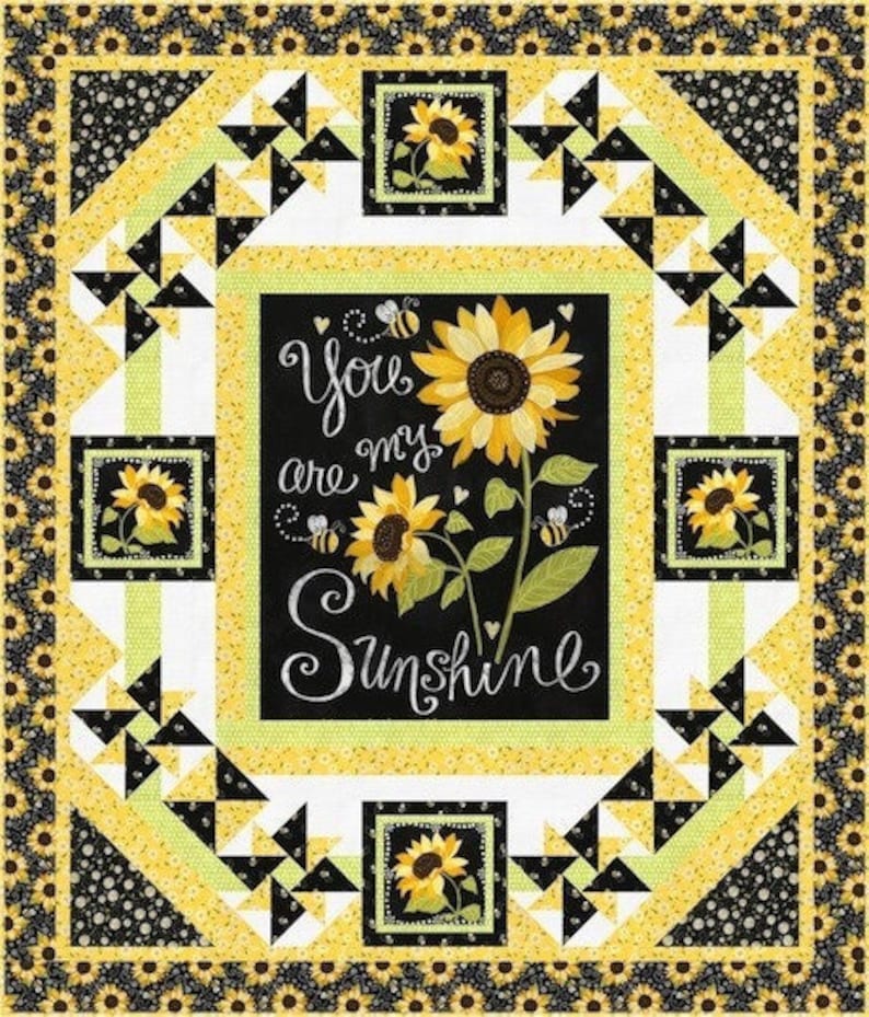 May include: A black and white quilt with a yellow border. The center of the quilt features a black panel with the text "You are my Sunshine" and a sunflower design. The quilt is made up of a repeating pattern of black and white triangles.