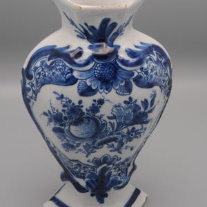 May include: A blue and white Delftware vase with a hexagonal base and a floral design.