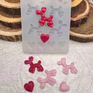 May include: A clear silicone mold with a balloon dog and heart design. Several finished resin balloon dogs and hearts in shades of pink and red are displayed next to the mold. The mold has a geometric pattern.