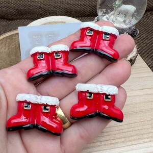 May include: Four red and white Santa boot ornaments with gold buckles. The boots are made of resin and have a glossy finish.