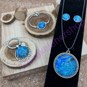 May include: A set of jewelry featuring a blue and white swirl design. The set includes a necklace, a bracelet, a keychain, and a pair of earrings.