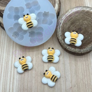 May include: A silicone mold with five bee-shaped cavities and four finished bee-shaped resin charms. The bees are yellow with black stripes and have white wings.