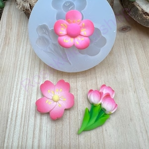 May include: Silicone mold for making pink and yellow flower cake decorations. The mold has a single flower design with five petals and a center circle. There are also two finished flower decorations, one with five petals and one with three petals.