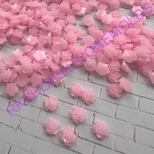 May include: A large quantity of pink resin rose and star shapes. The shapes are scattered on a white brick surface.