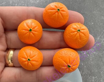 May include: Five small orange-colored silicone molds for making miniature orange fruit decorations. The molds are in a clear silicone sheet.  There are five miniature orange fruit decorations next to the molds.