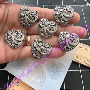 May include: Six silver heart-shaped charms with a floral design and a bow. The charms are displayed on a hand and a silicone mold.