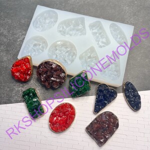 May include: A silicone mold with 10 different shapes for making resin jewelry. The mold is white and the shapes are clear. There are 10 finished resin pieces in various colors and shapes, including red, green, blue, and brown.