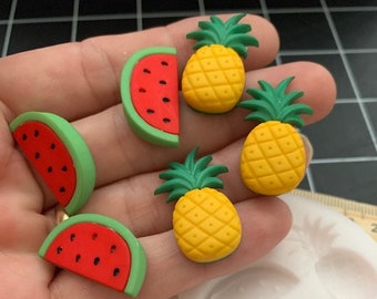 Puede incluir: Un molde de silicona para hacer rodajas de sandía y piña en miniatura. El molde tiene cuatro cavidades, dos para sandía y dos para piña. El molde es blanco y tiene una superficie lisa. El molde se muestra junto a una mano que sostiene rodajas de sandía y piña en miniatura hechas con el molde.