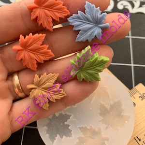 May include: Four silicone molds for making maple leaf shapes. The molds are shown with four finished resin maple leaves in different colors: orange, brown, green, and blue.