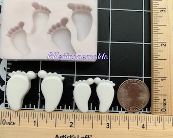 May include: White silicone mold with five baby footprints. The mold is on a gridded surface with a ruler and a US quarter for scale.