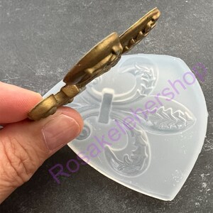 May include: A clear silicone mold with a raised design of a fleur-de-lis. The mold is used for making decorative items like cake toppers or fondant decorations.